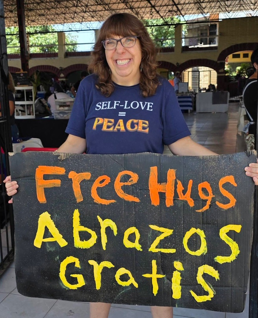 Sherry laughing while holding a hand painted Free Hugs, Abrazos Gratis sign at a market in Mexico
